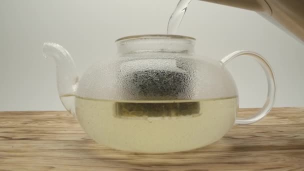 Verser de l'eau bouillante de la bouilloire dans une théière avec du thé blanc sur une table en bois 