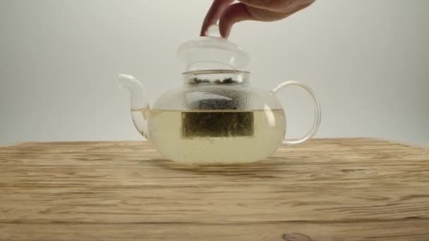 Thé blanc liquide dans une théière transparente, la main des hommes couvre le pot avec un capuchon 