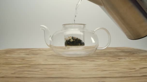 Pouring boiling water from kettle into white tea in a teapot on a wooden table — Stock Video