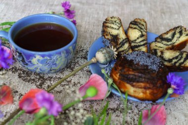 Güzel bir kahvaltı, bir fincan çay, haşhaş tohumu ve gelincik çiçekli taze börek..