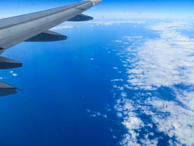 Uçak, beyaz bulutlarla çevrili olarak okyanusun üzerinde uçuyor..