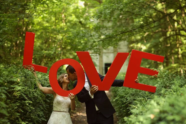 Casal de noivas alegre se divertindo com letras de amor na natureza — Fotografia de Stock