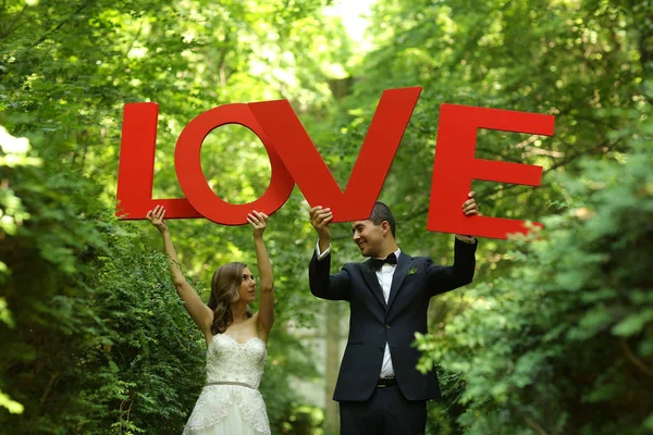 Casal de noivas alegre se divertindo com letras de amor na natureza — Fotografia de Stock