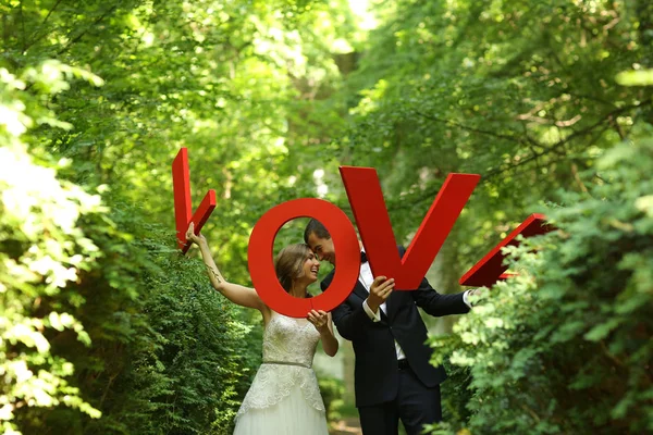 Joyful bridal couple having fun with LOVE letters in nature — Stock Photo, Image