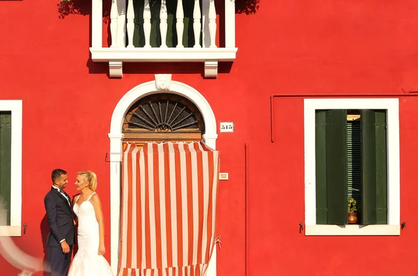 Bruden och brudgummen poserar framför ett rött hus — Stockfoto