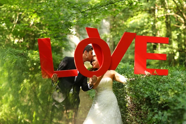 Beautiful bridal couple in the woods holding LOVE letters — Stock Photo, Image