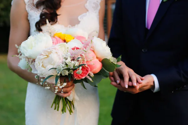 Γαμπρός και νύφη κρατώντας τα χέρια και γαμήλια ανθοδέσμη — Φωτογραφία Αρχείου