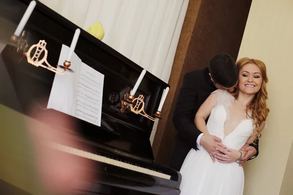 Noivo beijando sua noiva perto de piano — Fotografia de Stock