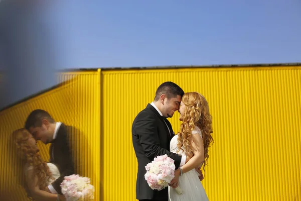 Pareja nupcial posando cerca de una pared amarilla —  Fotos de Stock