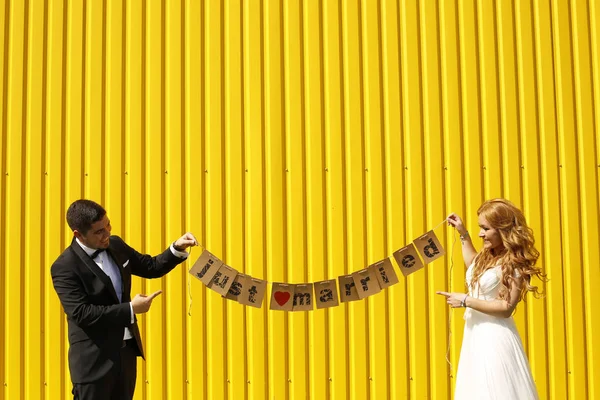 Coppia nuziale posa vicino a un muro giallo — Foto Stock