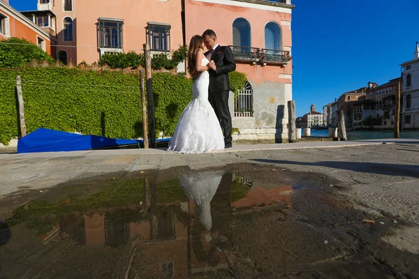 Bride and groom on the street, with reflection in water — Stock Photo, Image