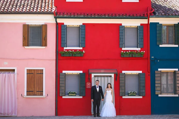 Noivo e noiva posando na frente de uma casa vermelha — Fotografia de Stock