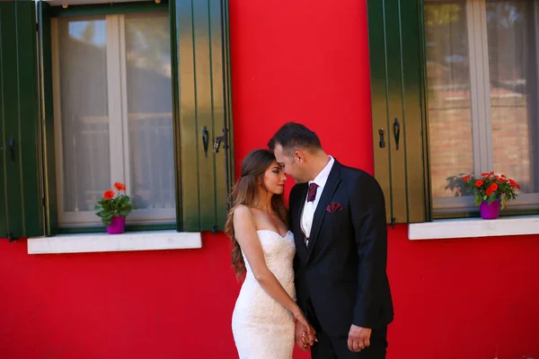 Brudgummen och bruden poserar framför ett rött hus — Stockfoto