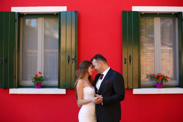 Marié et mariée posant devant une maison rouge — Photo