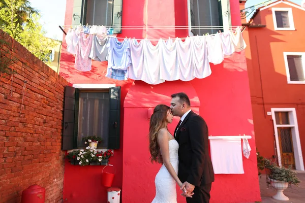 Noivo e noiva posando na frente de uma casa vermelha — Fotografia de Stock
