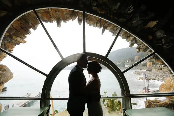 新郎和新娘剪影靠近窗户向大海 — 图库照片