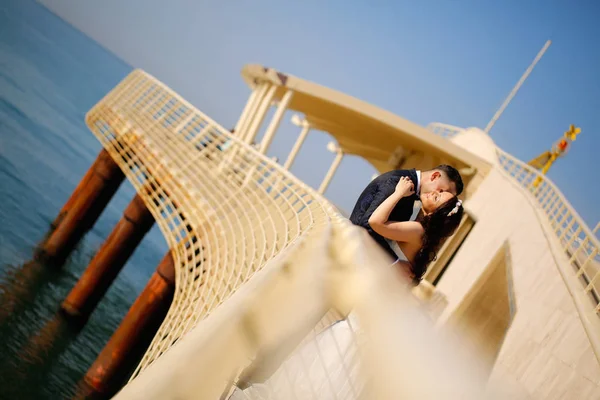 Sposo e sposa si baciano su un ponte vicino al mare — Foto Stock