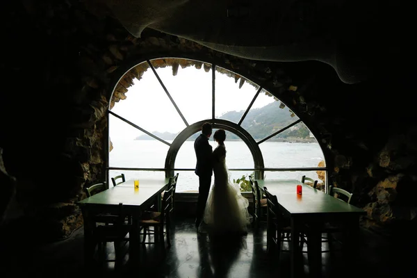 Γαμπρός και νύφη σιλουέτα κοντά σε ένα παράθυρο στη θάλασσα Royalty Free Εικόνες Αρχείου