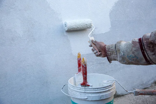 A hand with a paint roller and paint bucket painting the wall