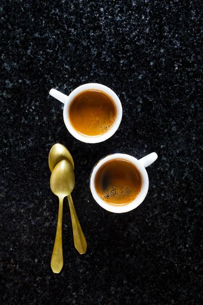 Två koppar färskt kaffe Espresso på svart marmor och två golden — Stockfoto