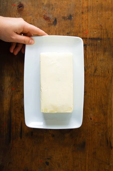 Trozo de mantequilla en un plato. mano femenina — Foto de Stock