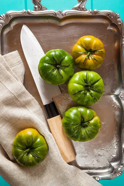 Grüne Tomaten auf einem silbernen Tablett und Kochmesser auf dem irisblauen Rücken — Stockfoto