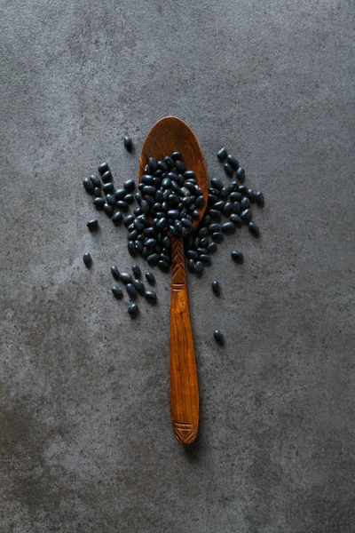 Frijoles negros en una cuchara de madera sobre un fondo oscuro — Foto de Stock