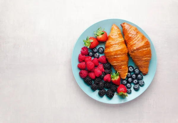 Mixed berries and croissants on a blue plate on a white backgrou — Stock Photo, Image