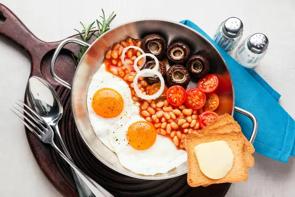 Breakfast with fried eggs in cast-iron pan, broken egg, tomatoes — Stock Photo, Image