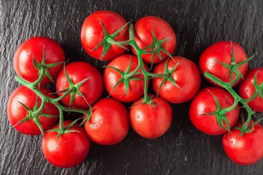 Bir yığın taze, olgun, lezzetli kırmızı domates siyah bir taşın üzerinde.