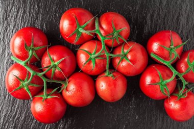 Bir yığın taze, olgun, lezzetli kırmızı domates siyah bir taşın üzerinde.