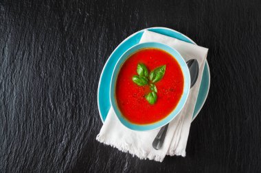 Siyah taş zemin üzerine mavi bir kapta domates çorbası. Üstten Görünüm. 