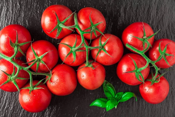 Un mucchio di pomodori rossi freschi, maturi e deliziosi su una pietra nera — Foto Stock