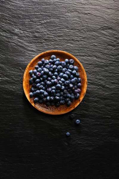 Pile of blueberries on a plate on a black stone background — Stock Photo, Image