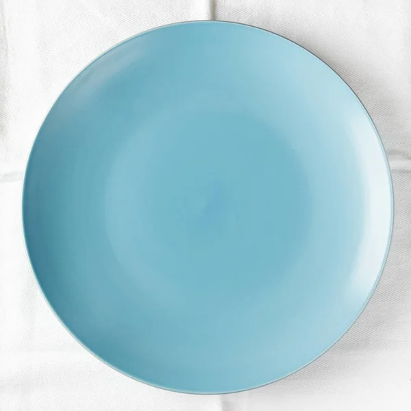 จานสีฟ้าว่างเปล่าบนผ้าปูโต๊ะสีขาว — ภาพถ่ายสต็อก
