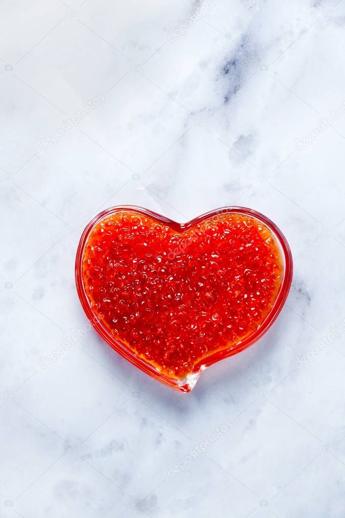 Red Caviar in a bowl in the form of a heart on a white marble ta