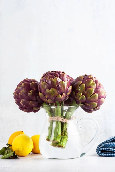 Fresh bunch of purple artichokes in a decanter with water on whi — Stock Photo, Image