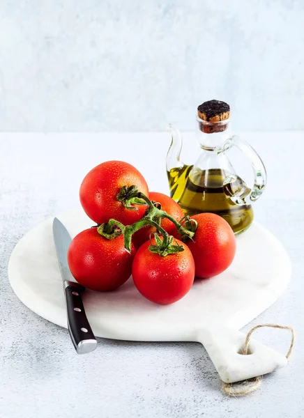 Ein Zweig frische reife nasse Tomaten und Olivenöl auf einem Tisch — Stockfoto