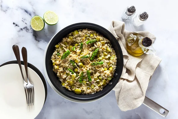 Risotto mit Spargel in einer Pfanne auf einem weißen Marmortisch. — Stockfoto