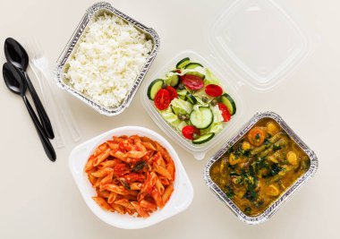 Tek kullanımlık konteynırlarda servis edilen yemekler: pirinç, sebze körisi, domates soslu İtalyan makarnası ve taze sağlıklı salata..