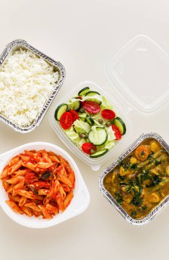 Tek kullanımlık konteynırlarda servis edilen yemekler: pirinç, sebze körisi, domates soslu İtalyan makarnası ve taze sağlıklı salata..
