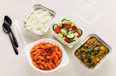 Tek kullanımlık konteynırlarda servis edilen yemekler: pirinç, sebze körisi, domates soslu İtalyan makarnası ve taze sağlıklı salata..