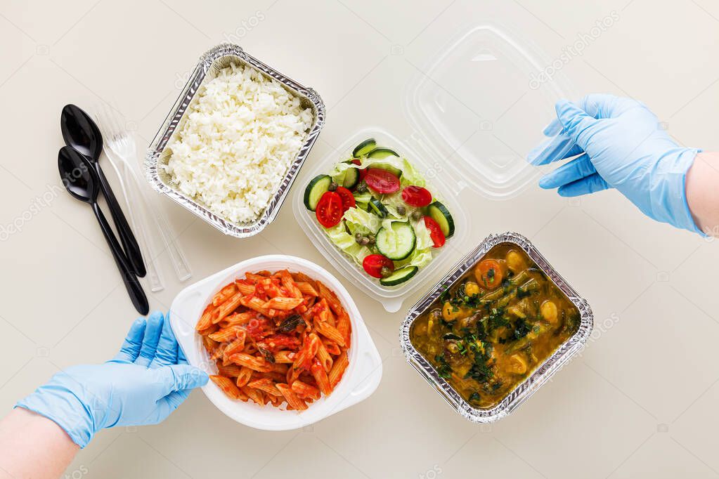 takeaway food in disposable containers: rice, vegetable curry, Italian pasta with tomato sauce and fresh healthy salad. and hands in medical surgical gloves. quarantine