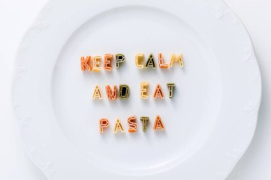 Deyimi CALM 'i koruyun ve beyaz bir tabakta çok renkli kuru makarnadan PASTA yiyin.