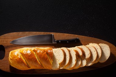 Kesme tahtasının üzerinde dilimlenmiş ekmek ve siyah bir arka planda şef bıçağı.