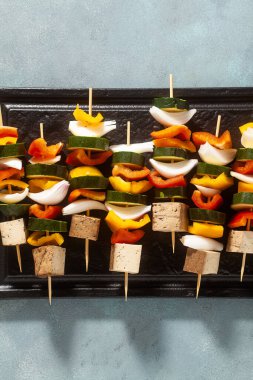 Vejetaryen sebze kebabı ve füme tofu, fırında pişirilmeye hazır, mavi arka planda.