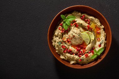 Ev yapımı patlıcan baba ganoush 'u nar tohumları, limon, zeytin yağı ve limon dilimleri ile siyah arka planda bir kaseye serpiştirdim.