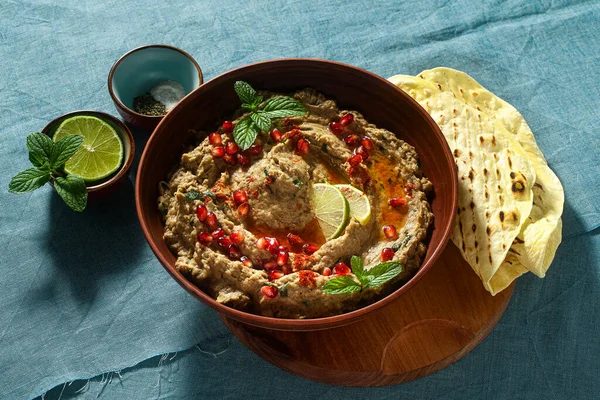 Ev yapımı patlıcan baba ganoush bir kâse içinde nar tohumu, limon, zeytin yağı ve limon dilimleri ile mavi keten masa örtüsü ve düz ekmek.