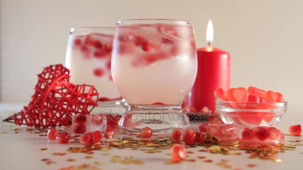 Romantik natürmort sorunsuz döngü. Saint Sevgililer günü kutlama. İki kadeh alkollü kokteyl ve buz, nar, kırmızı mum, el yapımı kalp ve şeker ile dekore edilmiştir. Yakın çekim. — Stok video