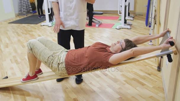 物理治疗师帮助老妇旋转的双腿，在健身房锻炼。健康的体操。积极的人. — 图库视频影像